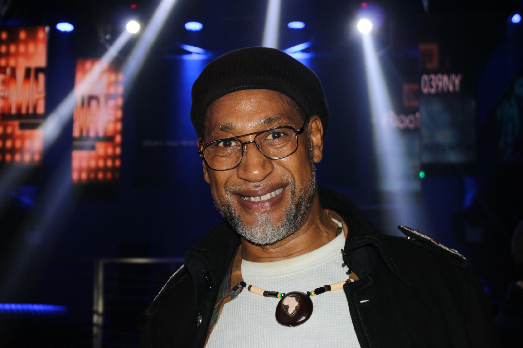 DJ Kool Herc smiling under stage lights, photographed by Stella Magloire